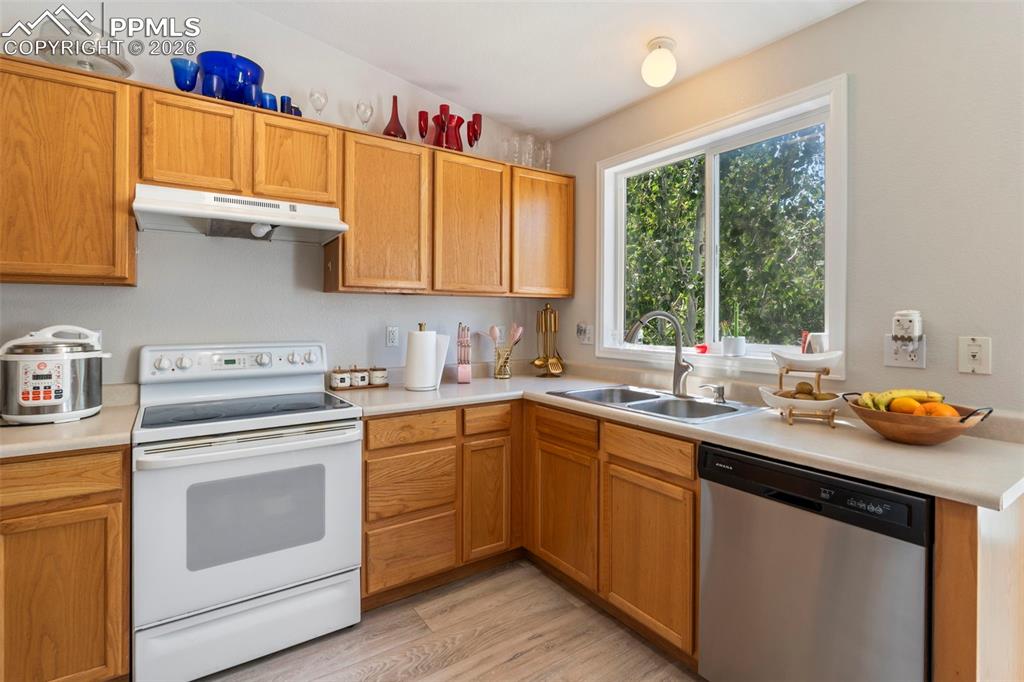 Kitchen featuring electric range, light countertops, dishwasher, under cabinet range hood, and light wood-type flooring