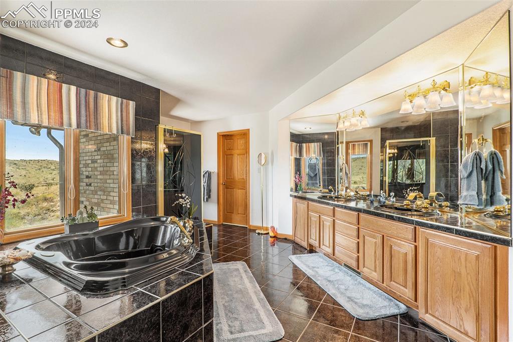 Bathroom with a relaxing tiled bath, tile flooring, vanity with extensive cabinet space, and a wealth of natural light