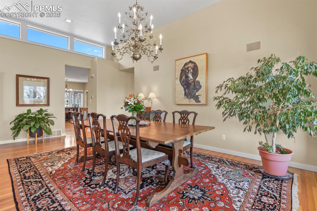 Dining room with light wood finished floors, chandelier, and high ceilings.   Looking through into the kitchen towards the eat-in area. 