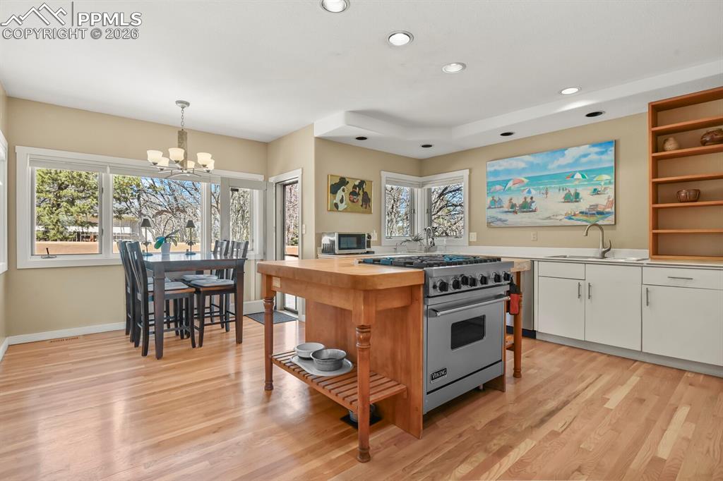 Spacious gourmet kitchen with white cabinetry, open shelves, 6-gas burner Viking cooktop and oven in the center island, double sink, hardwood floors, canned lighting, lots of windows, eat in area with door to the walled patio.