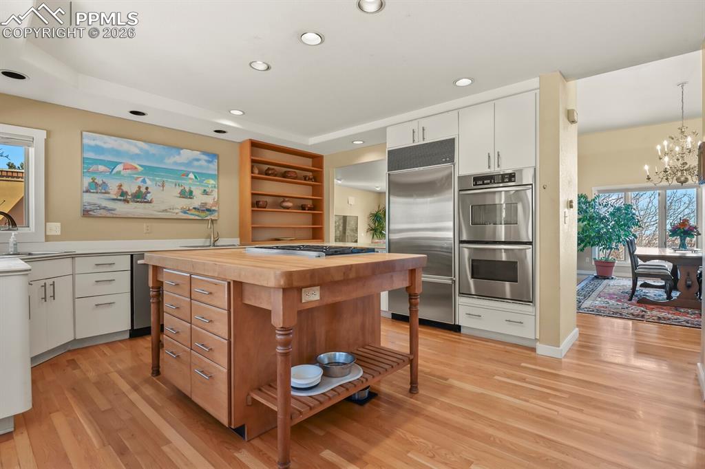 Kitchen with white cabinetry, open shelves, stainless steel double ovens, butcher block countertop with the 6-gas burners Viking Cooktop and Oven, hardwood floors and canned lights.
