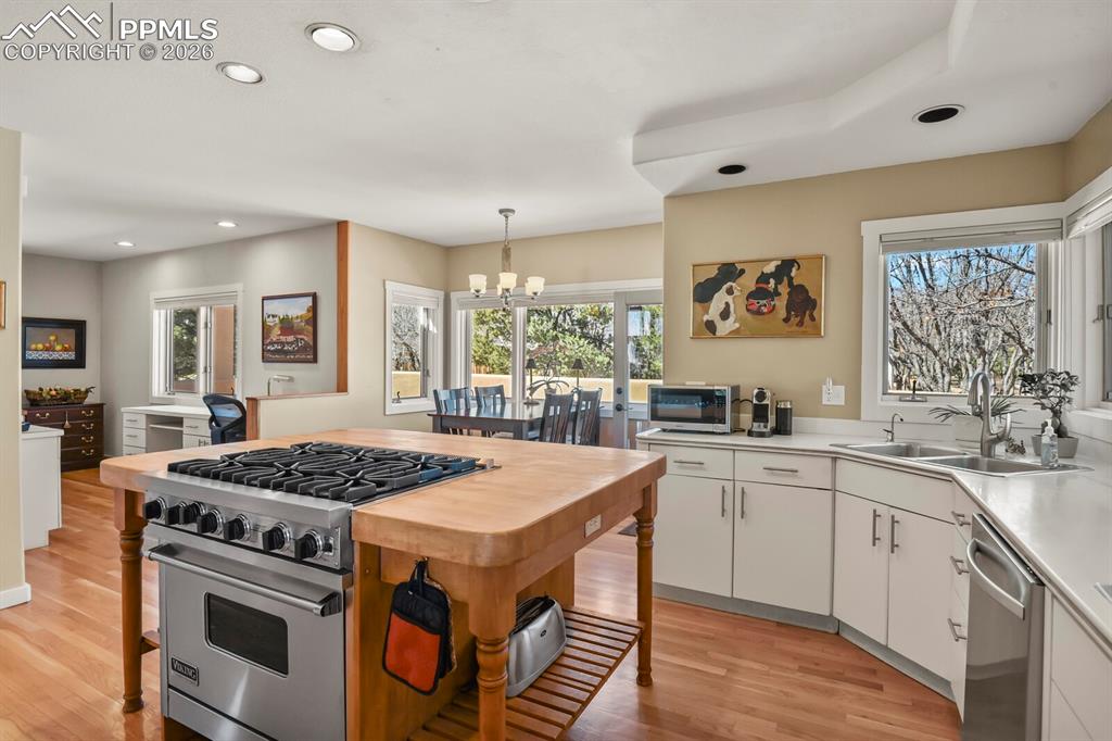 Kitchen with stainless steel appliances Viking gas hob and oven, showing the light filled eat-in kitchen table area with door to the outside walled patio.  Looking towards the large dedicated yet open plan office area.  