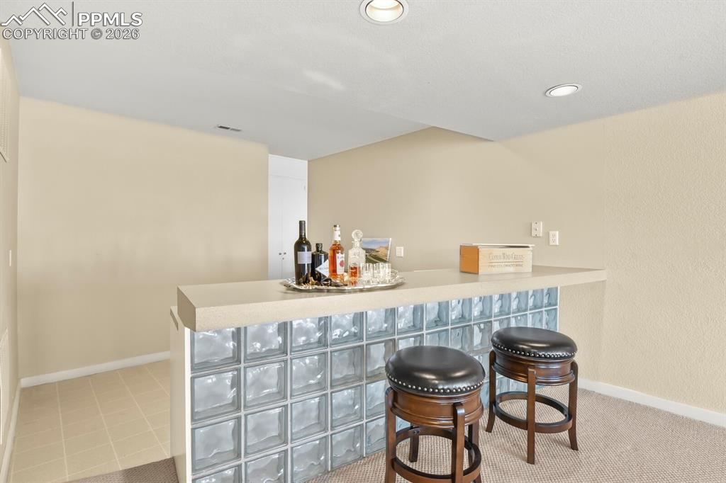 Indoor bar with light countertops and tiled area behind the bar and some recessed lighting.  Come and put your finishing touches on this area.