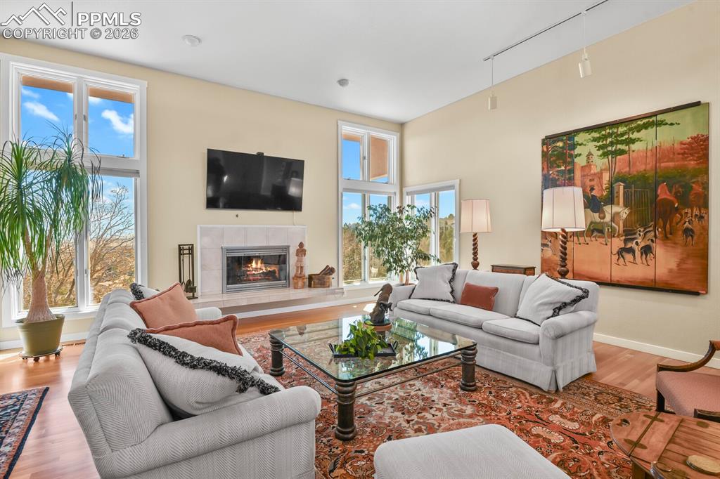 Living room with hardwood floors, wood burning fireplace and neutral surround, high ceilings and banks of windows for lots of natural light.