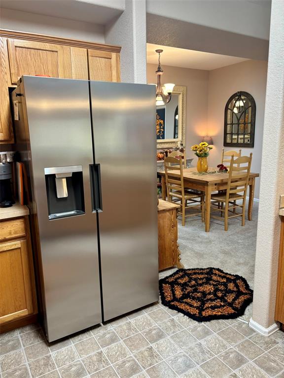 Kitchen featuring stainless steel fridge, brown cabinetry, light countertops, hanging light fixtures, and a textured wall