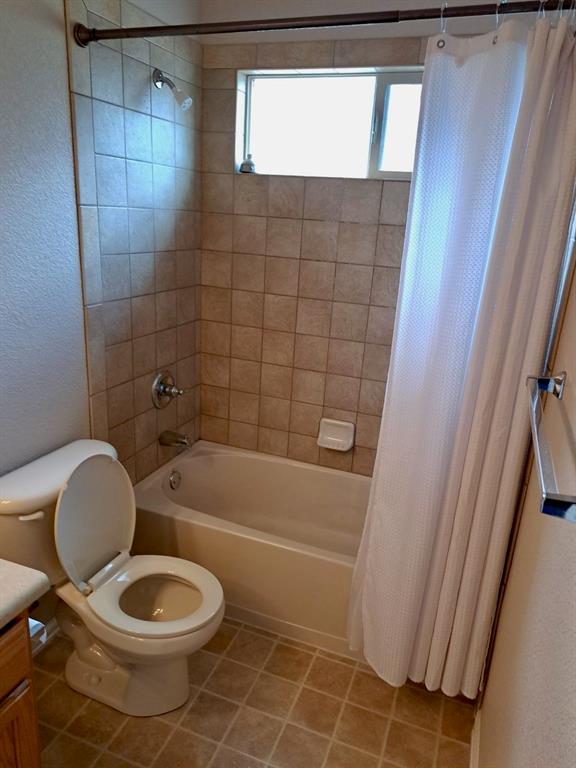 Bathroom featuring shower / bath combo with shower curtain, vanity, a textured wall, and tile patterned flooring