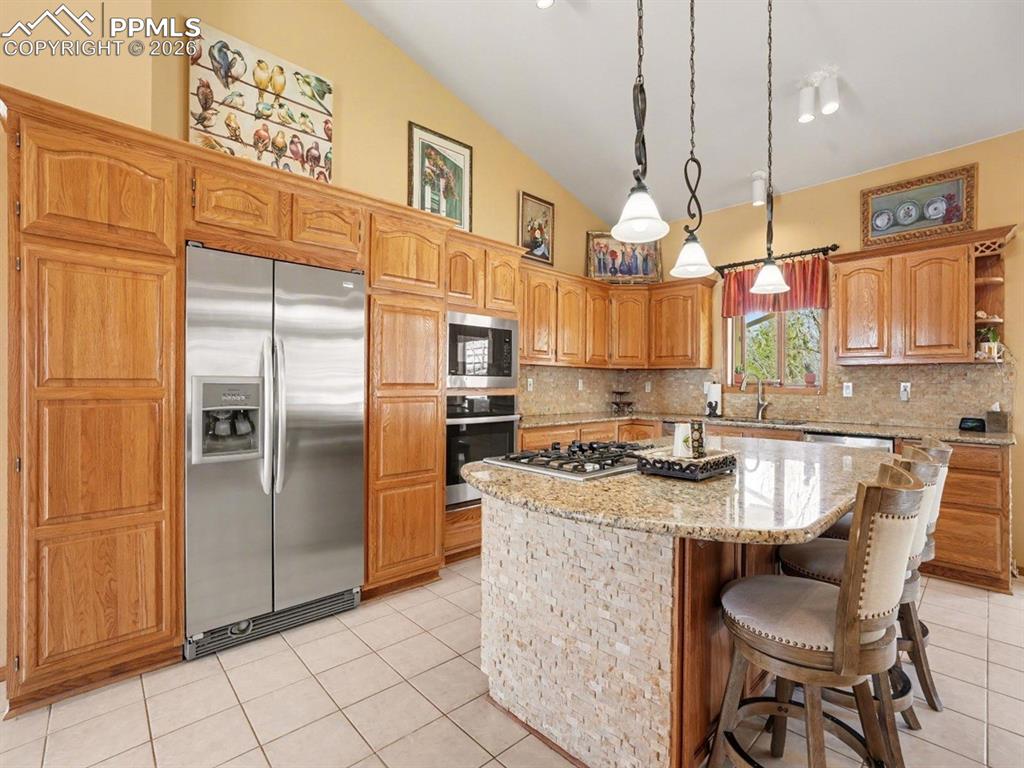Kitchen featuring stainless steel appliances, a kitchen island, light tile patterned floors, a breakfast bar area, and lofted ceiling