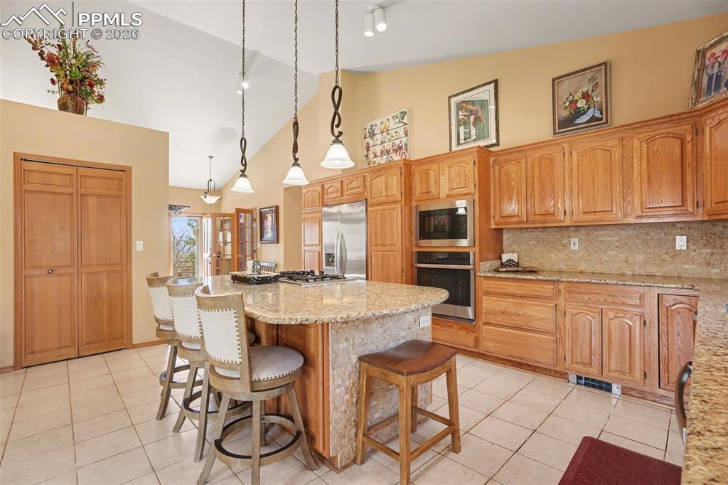 Kitchen with a kitchen breakfast bar, light stone countertops, built in appliances, pendant lighting, and a kitchen island