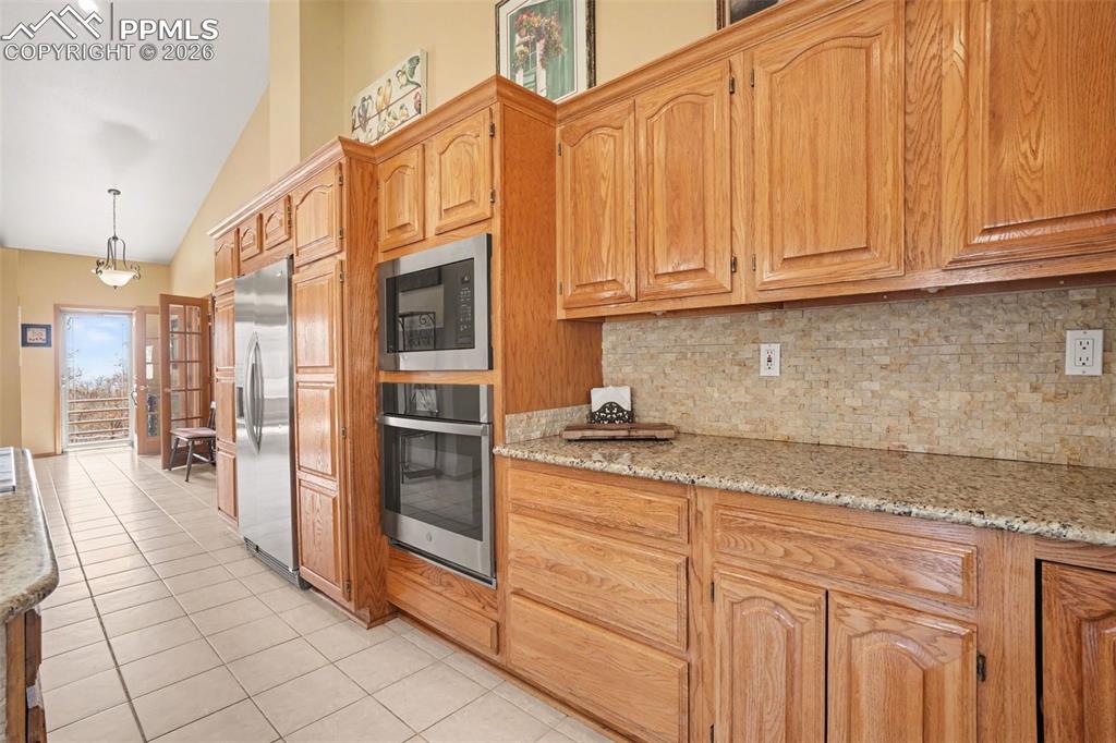 Kitchen with stainless steel appliances, light stone countertops, vaulted ceiling, light tile patterned floors, and backsplash
