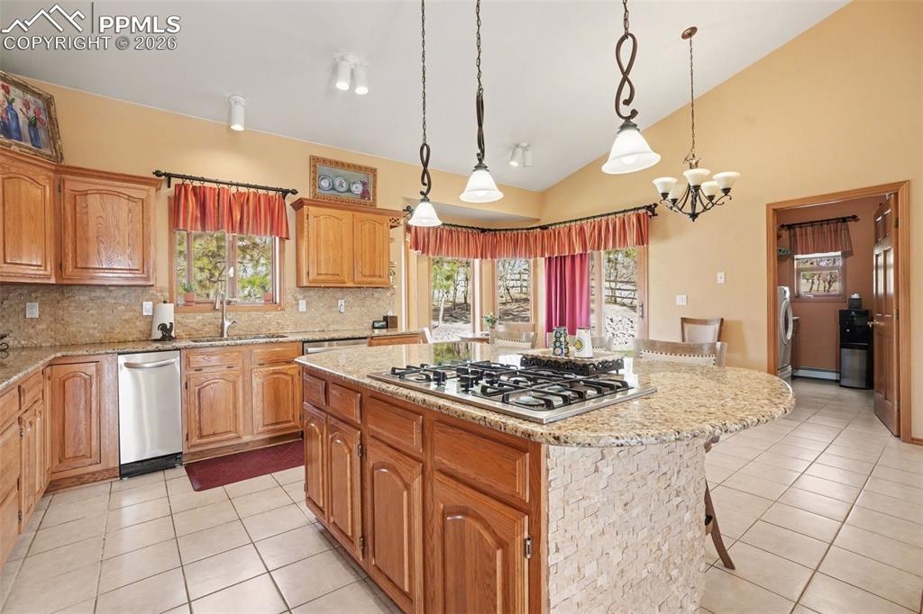 Kitchen with a kitchen island, light stone counters, vaulted ceiling, a breakfast bar area, and stainless steel gas stovetop
