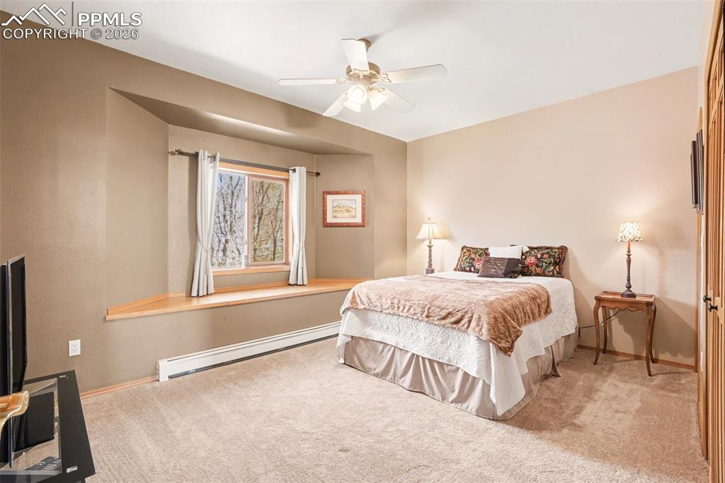 Bedroom with baseboard heating, light colored carpet, and ceiling fan