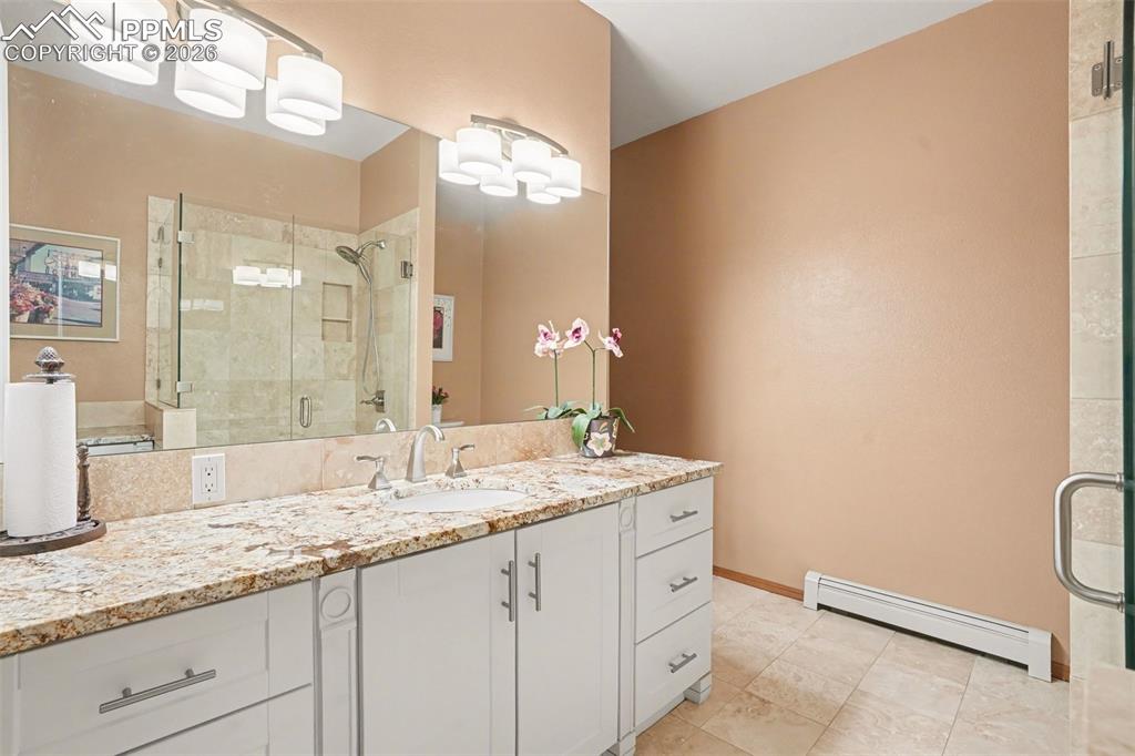 Full bathroom featuring a stall shower, baseboard heating, vanity, and light tile patterned flooring