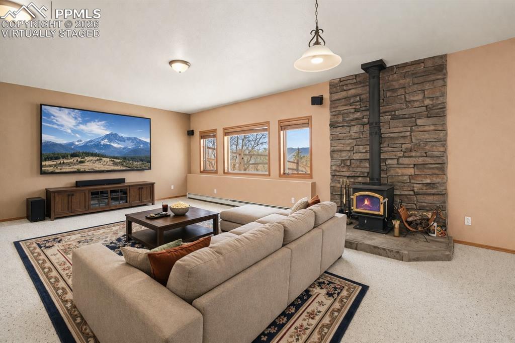 Virtually staged media or living room featuring a wood stove, a baseboard radiator, and carpet flooring