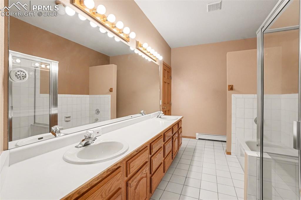Bathroom featuring double vanity, a garden tub, light tile patterned floors, a baseboard radiator, and a shower stall