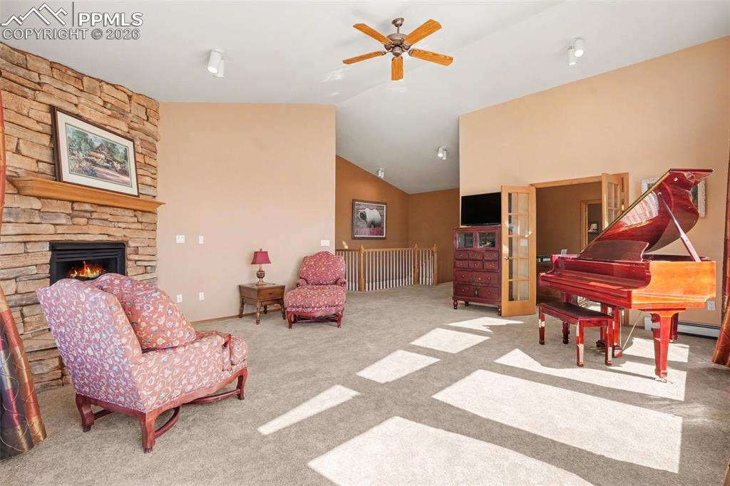 Living area featuring ceiling fan, vaulted ceiling, light carpet, and a fireplace