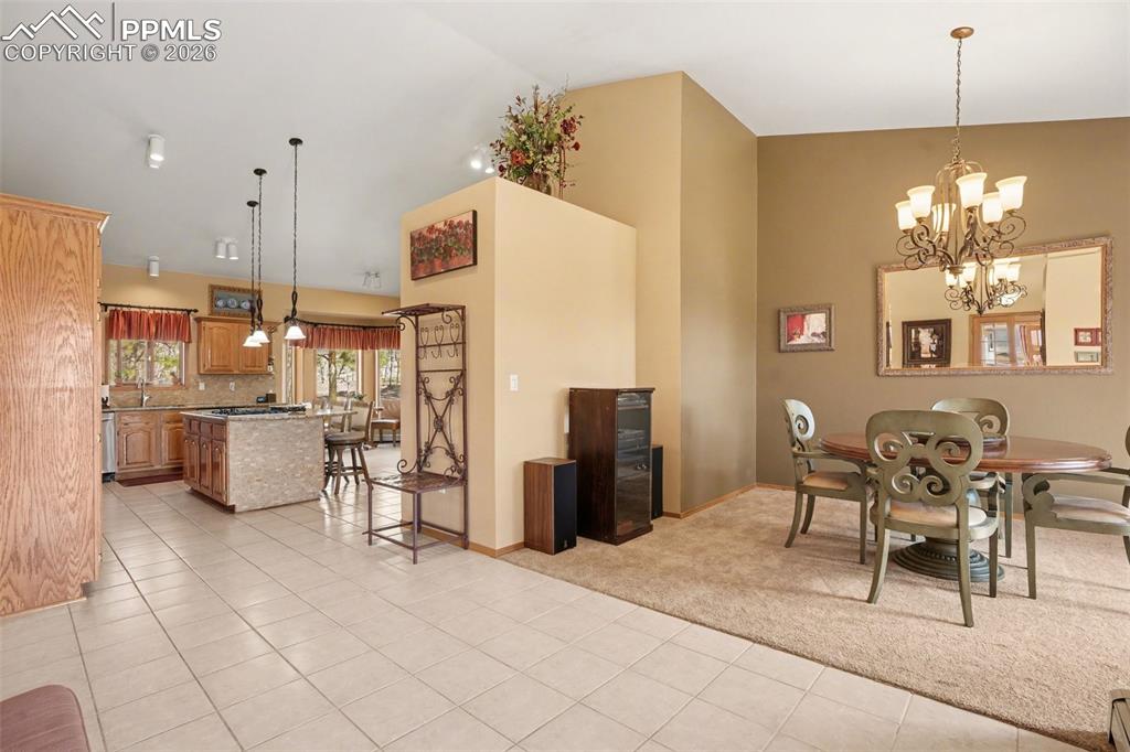 Dining room featuring hanging lights, light tile patterned flooring, lofted ceiling, and light colored carpet