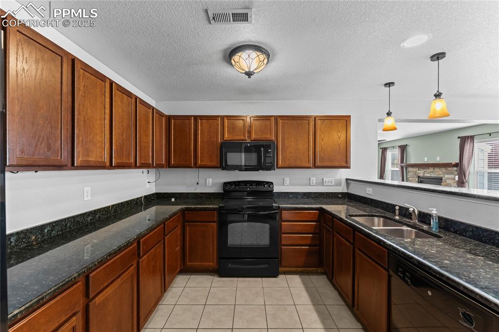 Kitchen featuring black appliances, decorative light fixtures, dark stone countertops, a textured ceiling, and light tile patterned floors