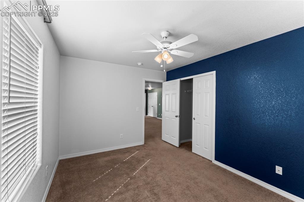 Unfurnished bedroom featuring dark colored carpet, ceiling fan, and a closet
