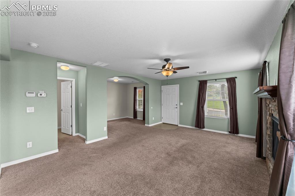 Unfurnished living room with arched walkways, carpet floors, a stone fireplace, and a ceiling fan