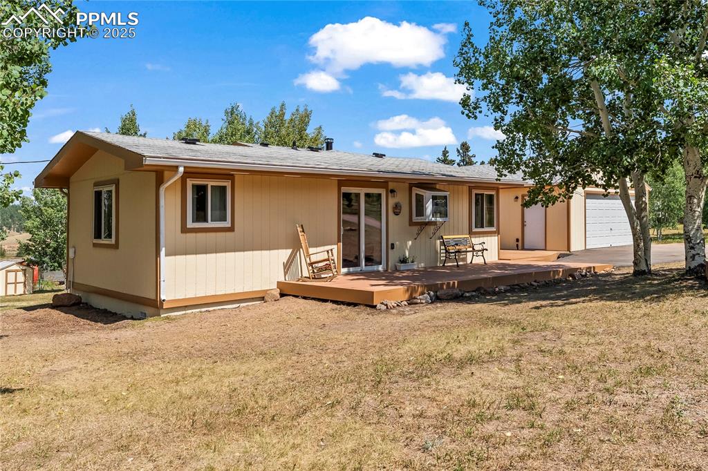 Front view of property featuring a yard, a garage, a deck, and roof with shingles