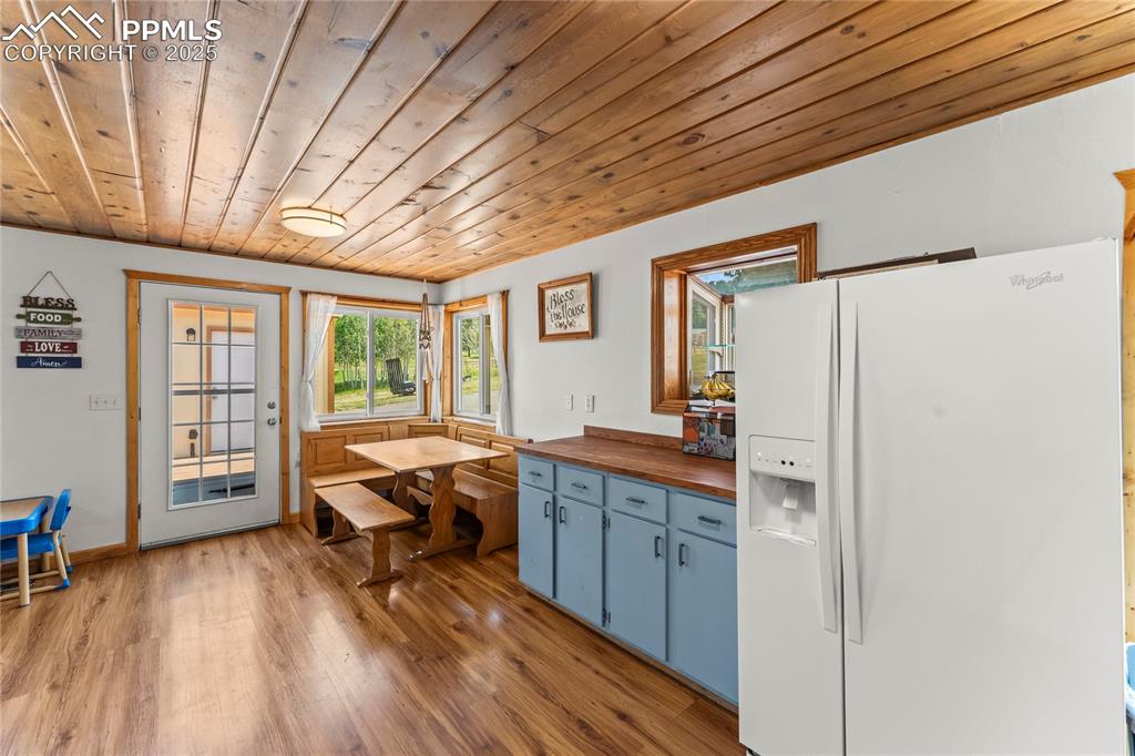 Kitchen with butcher block countertops, white fridge with ice dispenser, wooden ceiling, light wood-style flooring, and blue cabinets