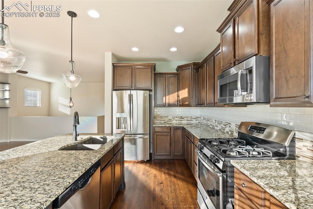 Kitchen featuring stainless steel appliances, decorative light fixtures, light stone counters, dark wood finished floors, and backsplash