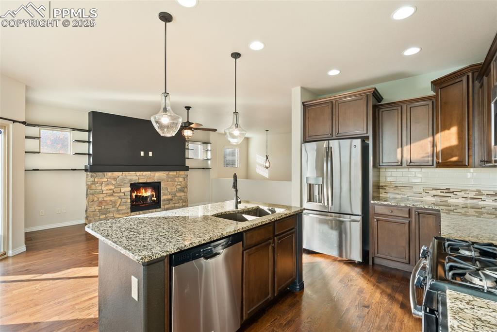 Kitchen featuring appliances with stainless steel finishes, light stone countertops, a fireplace, tasteful backsplash, and pendant lighting