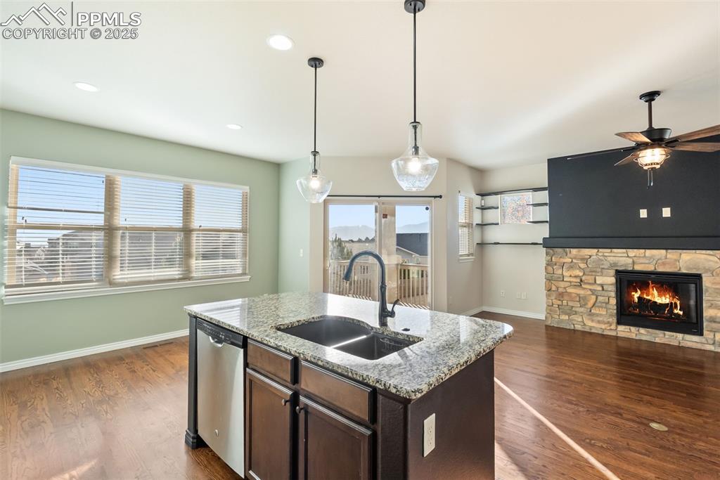 Kitchen featuring light stone counters, dark brown cabinetry, dark wood-type flooring, stainless steel dishwasher, and open floor plan