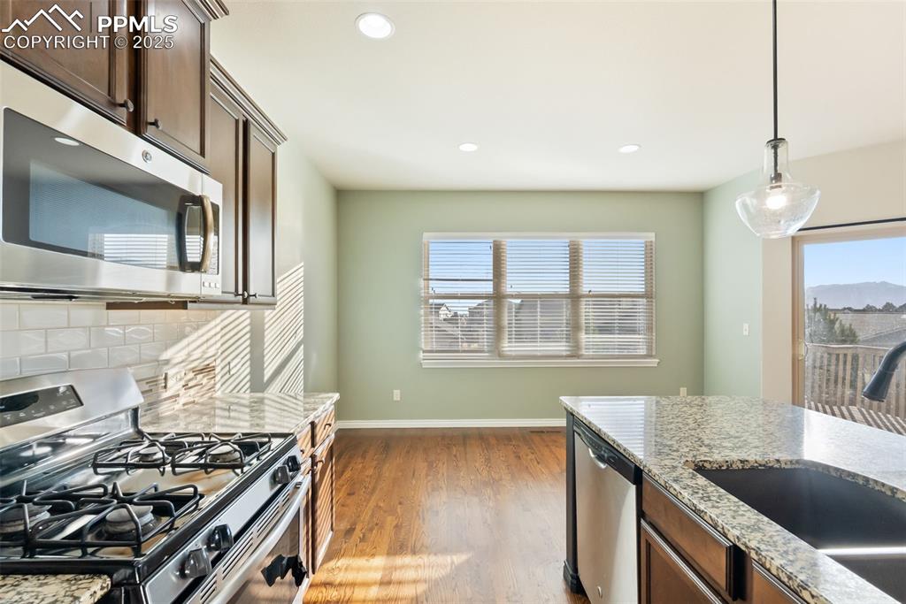 Kitchen featuring appliances with stainless steel finishes, light stone countertops, backsplash, decorative light fixtures, and light wood-style floors