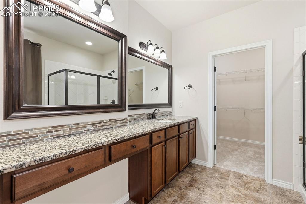 Full bath featuring vanity, a shower stall, a walk in closet, and tasteful backsplash