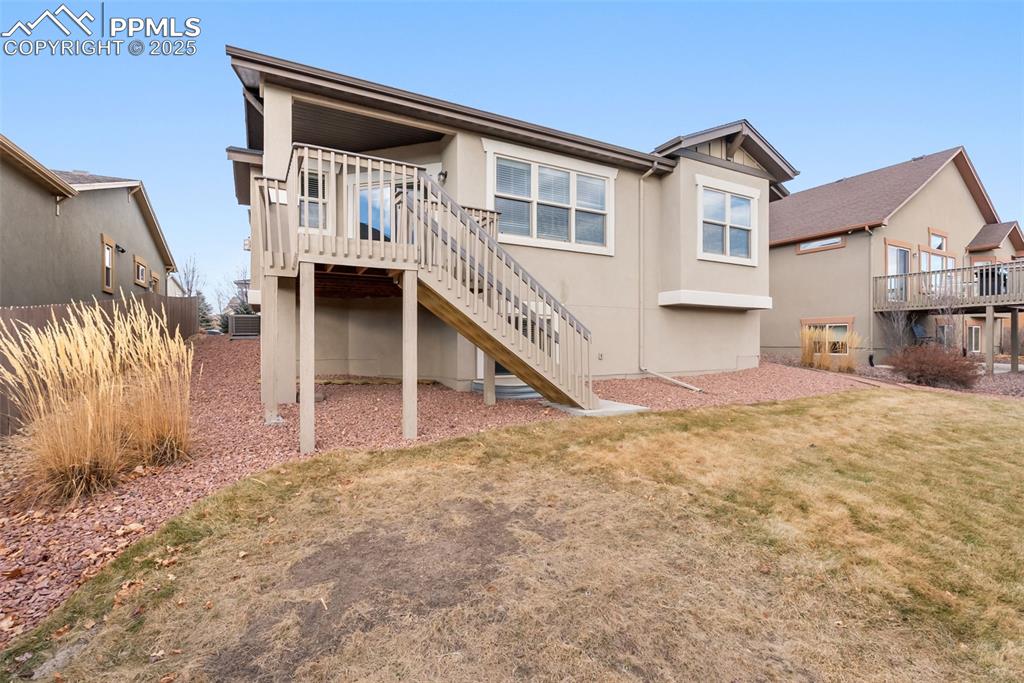 Rear view of property featuring stucco siding, stairs, and a lawn