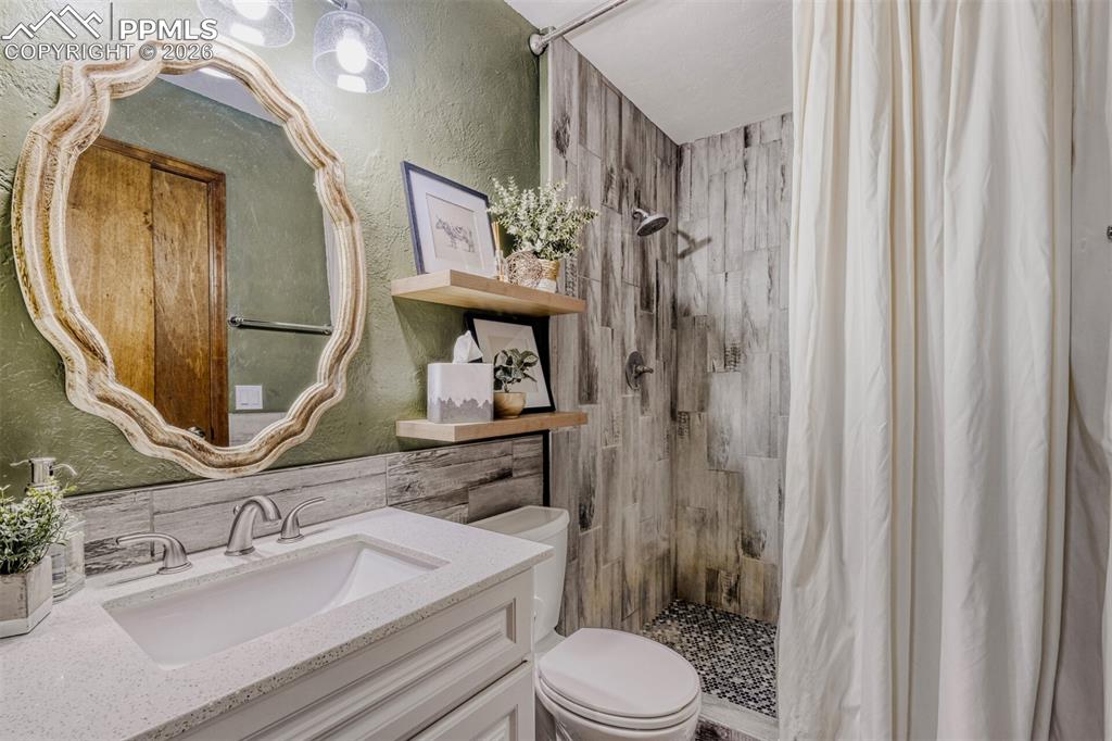 Full bathroom featuring a textured wall, a stall shower, and vanity