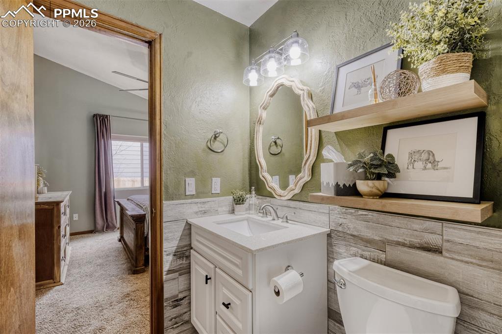 Bathroom featuring vanity, a textured wall, ensuite bathroom, tile walls, and a wainscoted wall