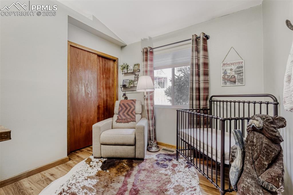 Bedroom featuring light wood-style flooring, lofted ceiling, a nursery area, and a closet