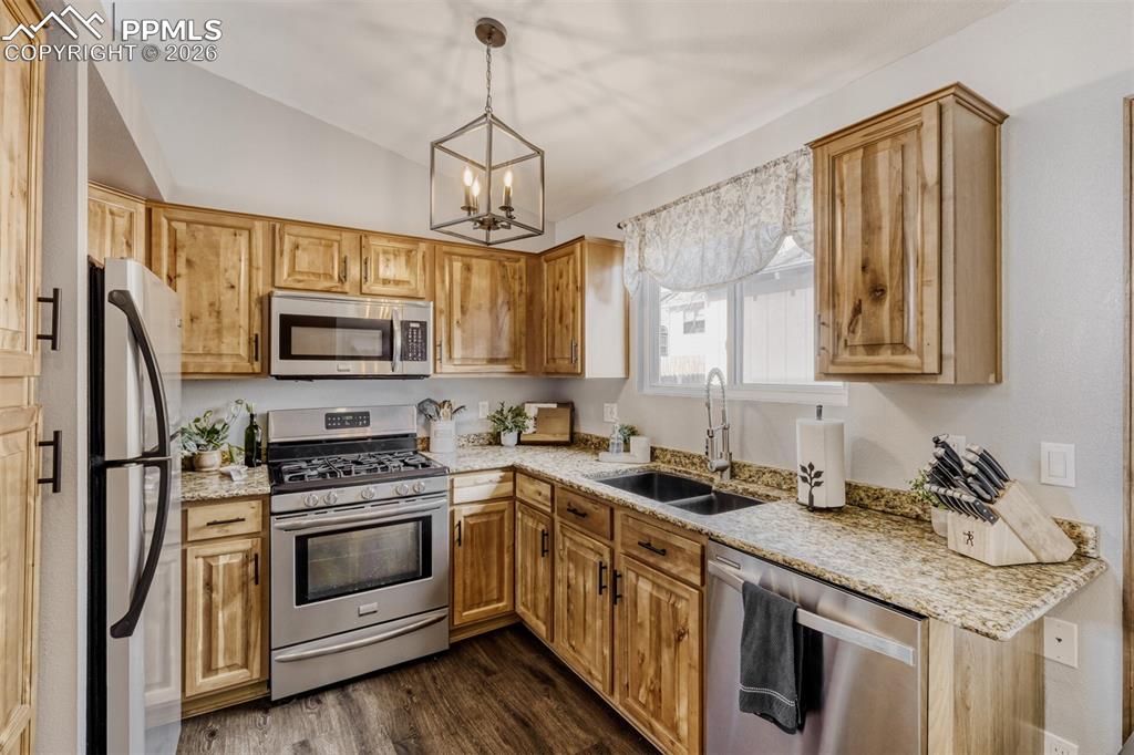 Kitchen with stainless steel appliances, light stone counters, vaulted ceiling, dark wood-style floors, and suspended lighting