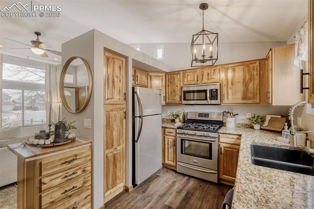Kitchen featuring stainless steel appliances, ceiling fan, dark wood finished floors, a chandelier, and light stone countertops