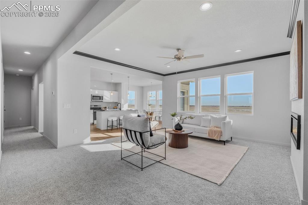 Living area with light carpet, a glass covered fireplace, a ceiling fan, crown molding, and recessed lighting