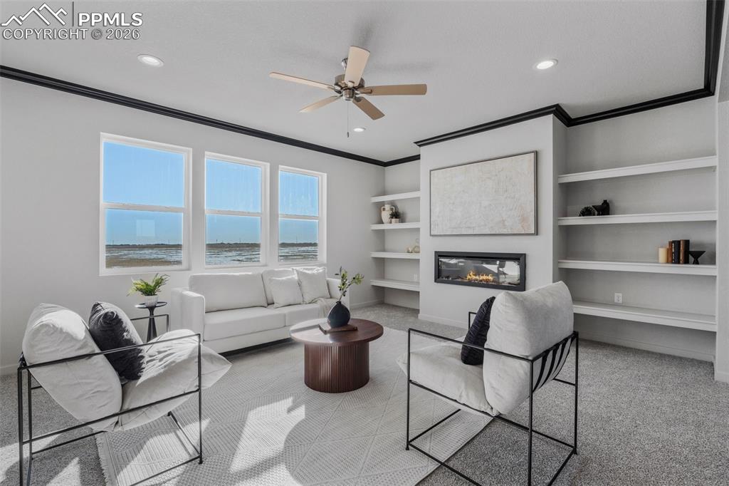 Living room with light carpet, built in shelves, a glass covered fireplace, ceiling fan, and ornamental molding