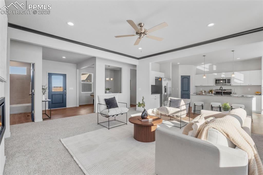 Living area with a ceiling fan, light carpet, a glass covered fireplace, recessed lighting, and a chandelier