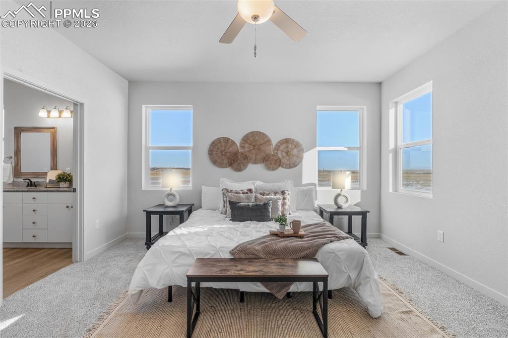 Bedroom with light colored carpet, ceiling fan, and connected bathroom