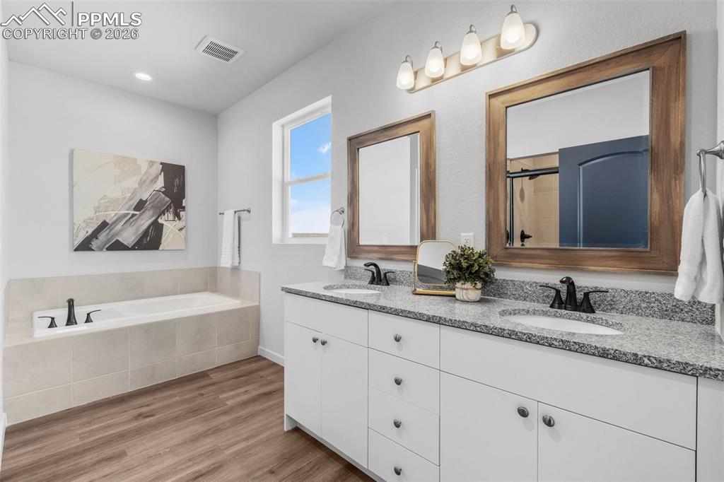 Bathroom with double vanity, a bath, light wood-style floors, and an enclosed shower