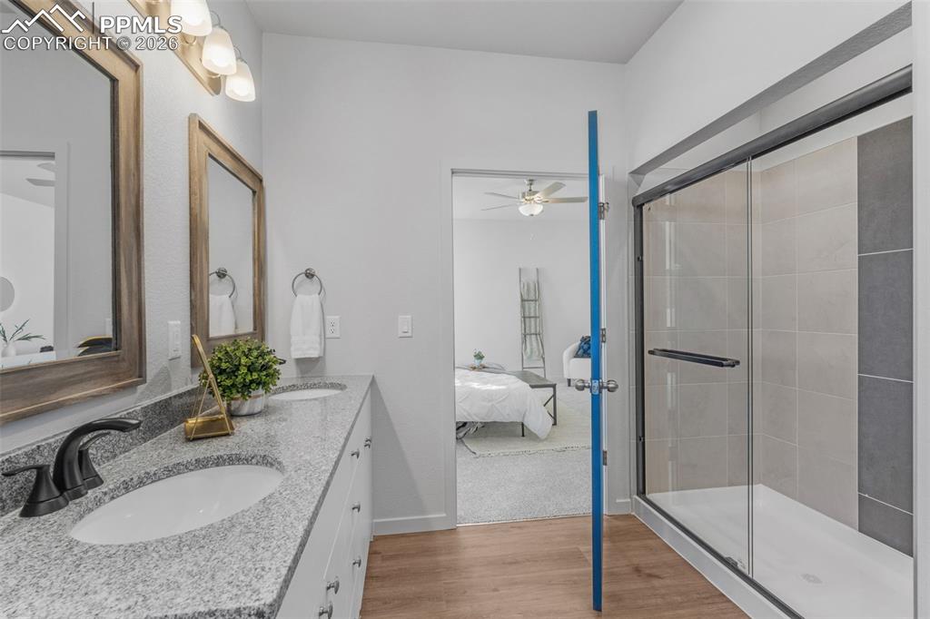 Bathroom with a shower stall, light wood finished floors, double vanity, and ensuite bathroom