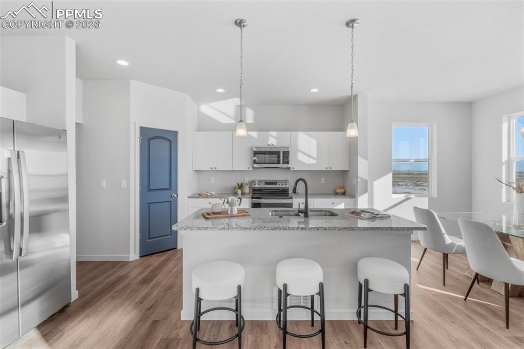 Kitchen with stainless steel appliances, white cabinetry, a center island with sink, light stone counters, and light wood-style flooring