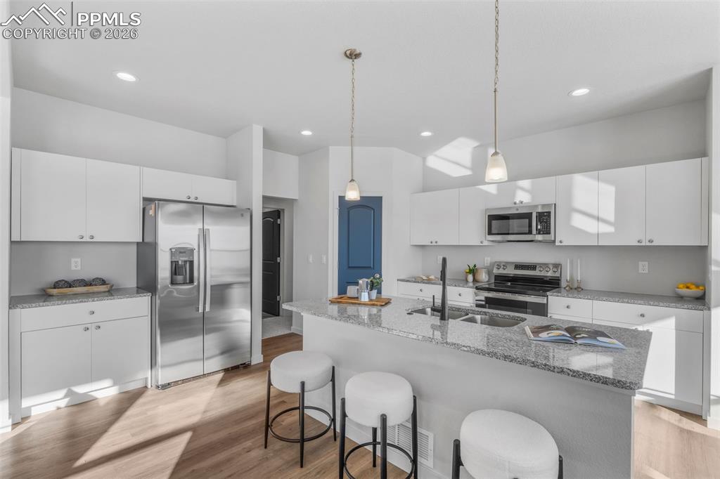 Kitchen with appliances with stainless steel finishes, white cabinetry, a breakfast bar area, light wood-style floors, and light stone counters