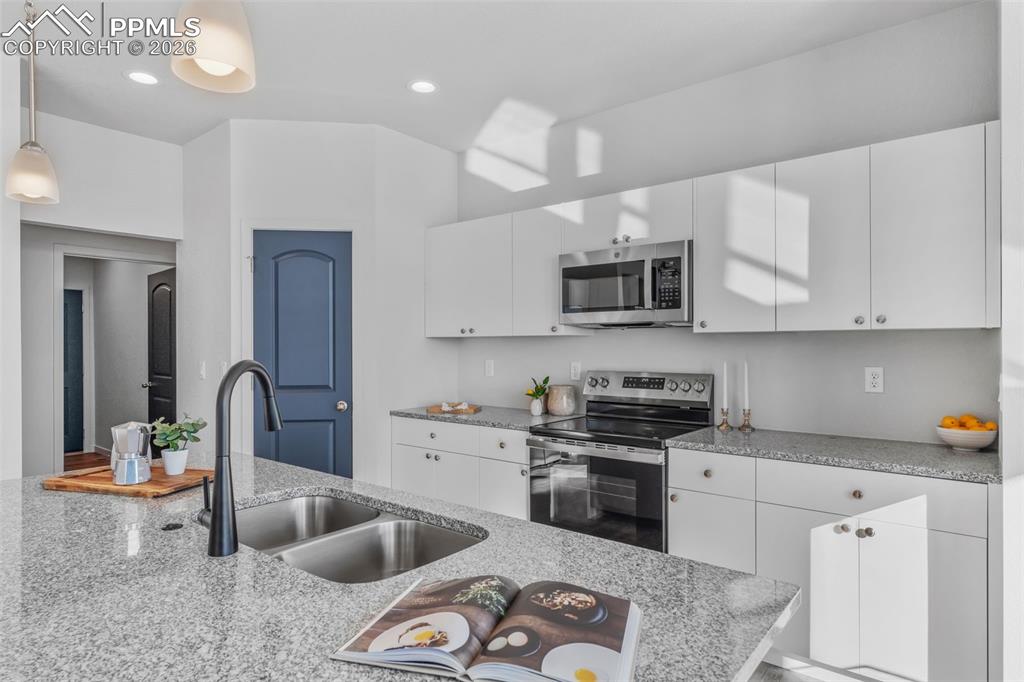 Kitchen featuring stainless steel appliances, white cabinets, light stone countertops, pendant lighting, and recessed lighting