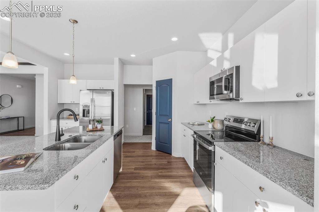 Kitchen featuring appliances with stainless steel finishes, white cabinetry, light stone counters, dark wood-style flooring, and pendant lighting