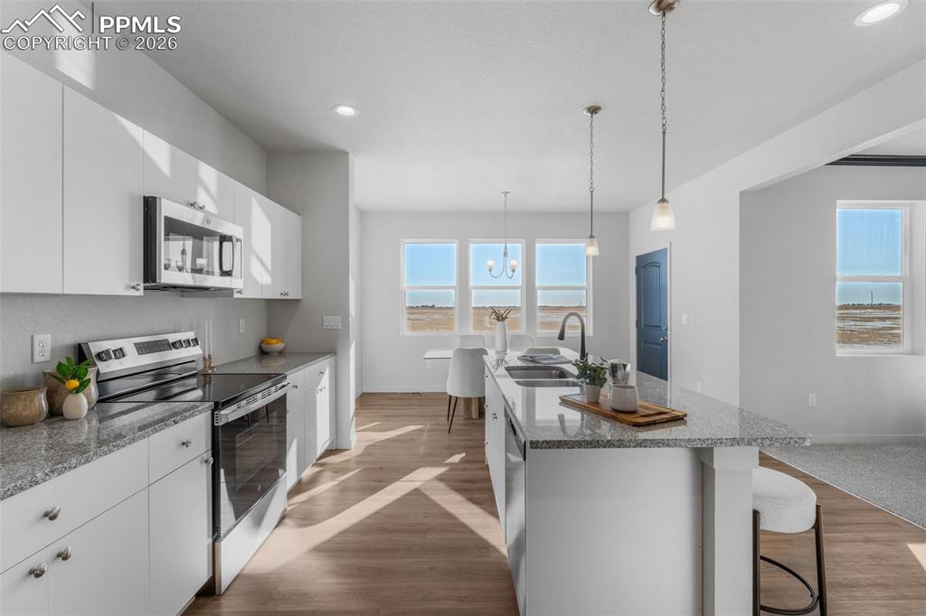 Kitchen featuring stainless steel appliances, a breakfast bar, white cabinets, light stone countertops, and a kitchen island with sink