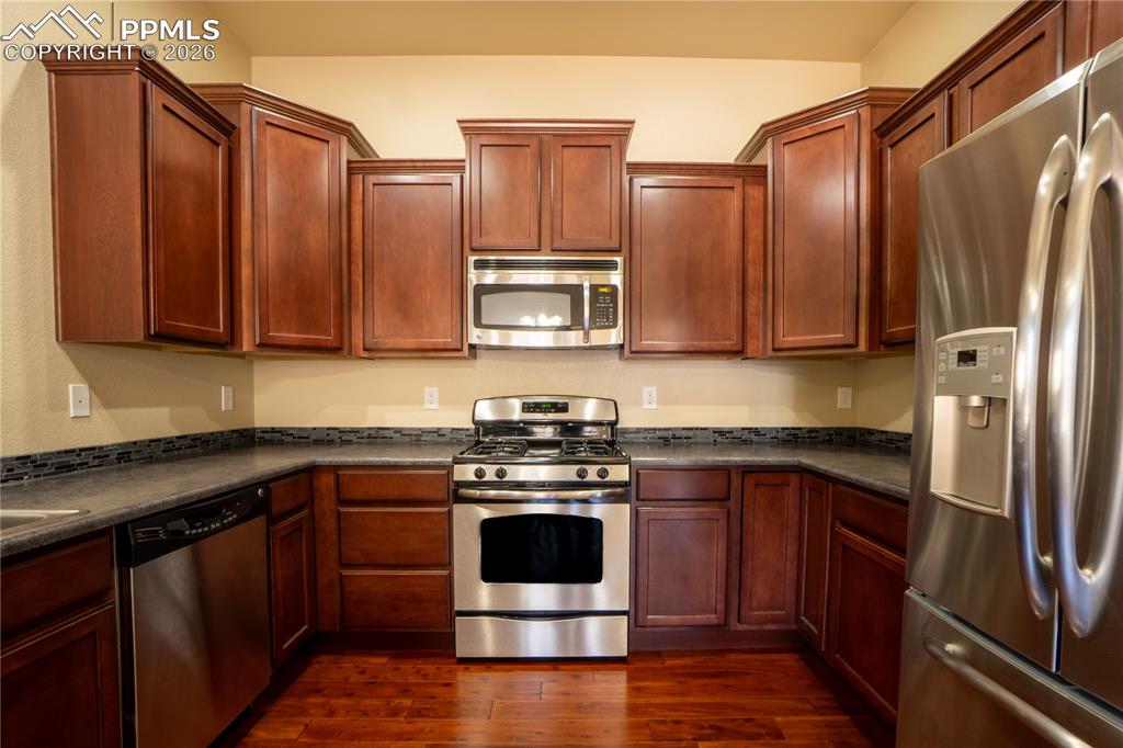 Kitchen with stainless steel appliances, dark countertops, and dark wood finished floors