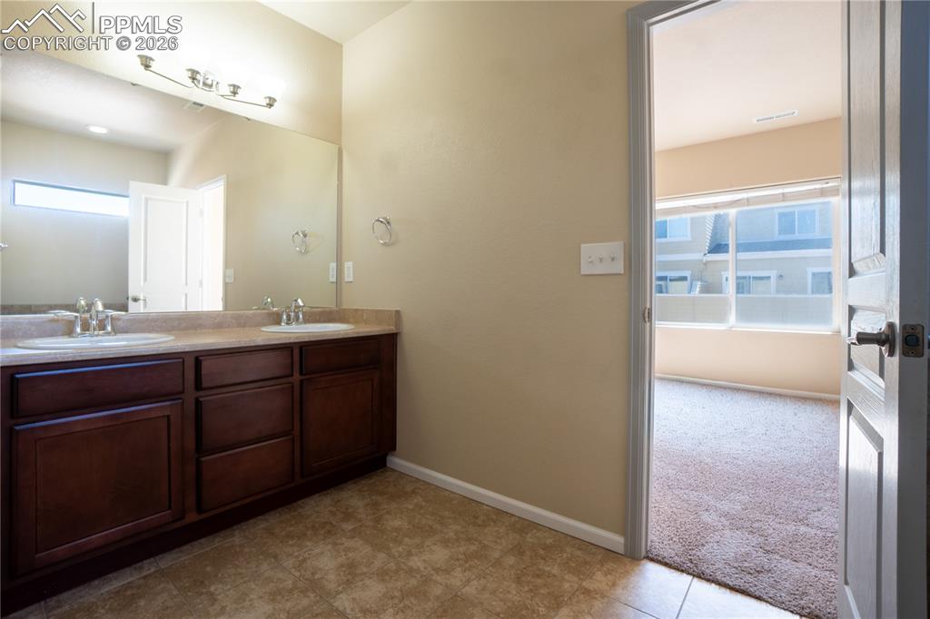 Full bathroom with double vanity, plenty of natural light, and light colored carpet