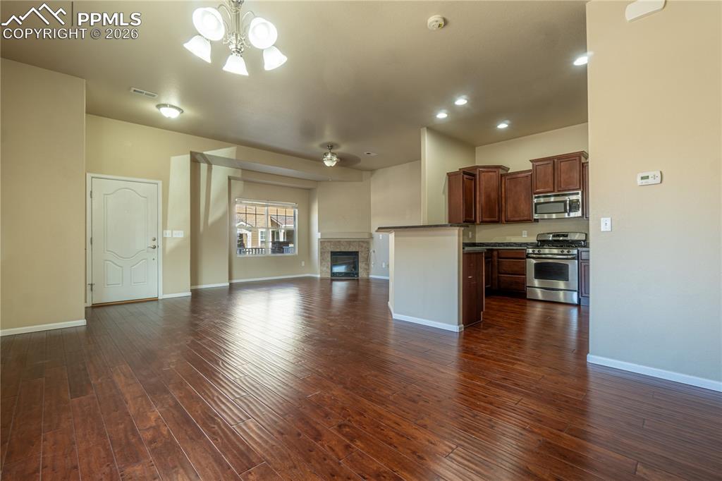 Unfurnished living room with a fireplace, dark wood-style flooring, a ceiling fan, and suspended lighting